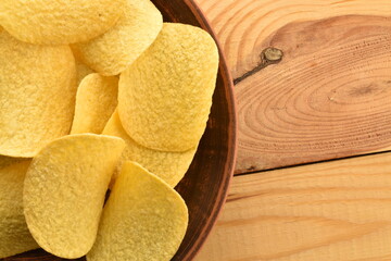 Several potato chips on a clay dish on a wooden table, close-up, top view.