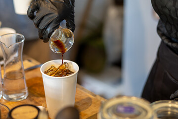 selective focus white paper cups A coffee shop worker wearing black rubber gloves is pouring a shot of black coffee into a paper cup. for customers to buy back