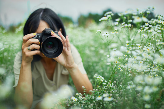 Portrait of Female photographer take photo outdoors on flower field landscape holding a camera
