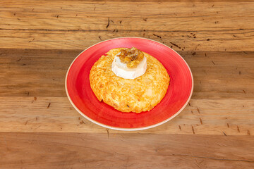 Large potato omelette with goat cheese and caramelized onion on a red plate and wooden table