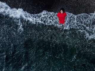 top view of a woman in a red dress looking at the camera with sea foam background
