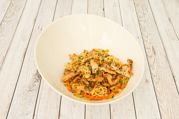Chicken yakisoba noodles sautéed with vegetables and poppy seeds, sesame seeds and chopped chives on a white table.