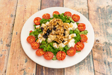 salad with chopped cherry tomatoes, diced fresh cheese, hearty chunks of walnuts and raisins on lamb's lettuce shoots.