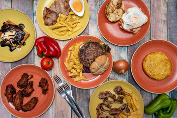 set of dishes of conventional Spanish food. Lamb chops, potato omelette, beef fillet with homemade fries, waffle with vanilla ice cream, xl hamburger with potatoes.