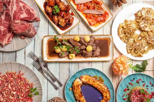 Top view image of sophisticated dishes of Spanish gastronomy. Grilled octopus with purple mayonnaise, Steak with round potatoes, fried artichoke hearts.