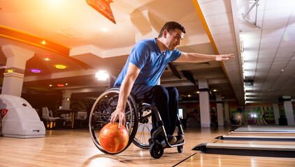 Young disabled man in wheelchair playing bowling in the club