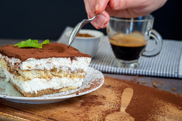 woman eating traditional tiramisu cake using a spoon. Authentic gluten-free Italian layered dessert with ladyfinger biscuits, mascarpone cheese cream and cocoa powder. Cup of coffee in the background.