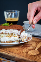woman eating traditional tiramisu cake using a spoon. Authentic gluten-free Italian layered dessert with ladyfinger biscuits, mascarpone cheese cream and cocoa powder. Cup of coffee in the background.