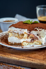 Slice of eaten traditional tiramisu cake with a cup of coffee in the background. Authentic gluten-free Italian layered dessert with ladyfinger biscuits, mascarpone cheese cream and cocoa powder. Side