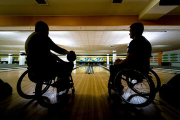 Two young disabled men in wheelchairs playing bowling in the club