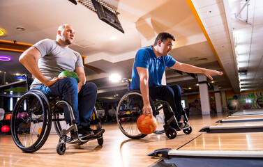 Fototapeta na wymiar Two young disabled men in wheelchairs playing bowling in the club