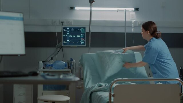 Nurse making bed in hospital ward preparing room for pacient with disease. Arranging pillow and blanket at medical facility for health problems. Modern equipment for illness treatment