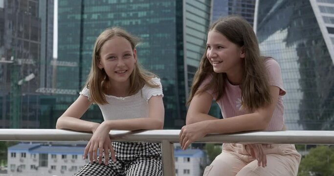 Two teenager girl talking on urban skyscrapers background in modern city. Portrait girl teenager on urban architecture landscape