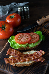 Close up of an open faced toasted bacon and tomato sandwich on a wooden board, ready for eating.
