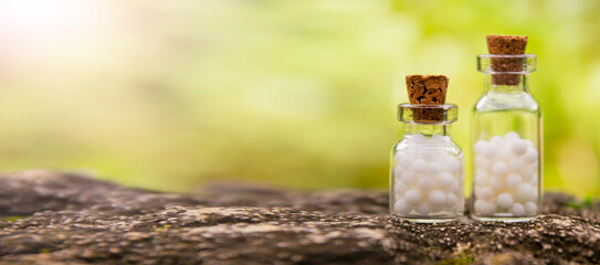 Homeopathic balls in bottles on the background of nature. Homeopathy alternative medicine concept. Side view, place for text.