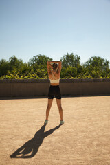 young athlete on her back doing an outdoor warm-up exercise with her full shadow on the ground