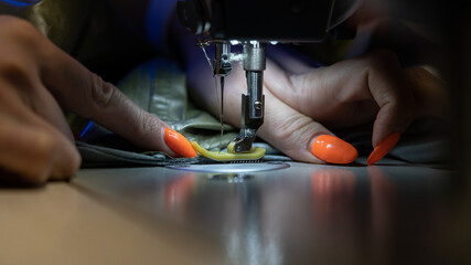 Woman tailor work on sewing machine stitching patterns of new collection. Closeup shot of female sewer hand dressmaking. Seamstress use professional equipment for tailoring. Garment industry concept