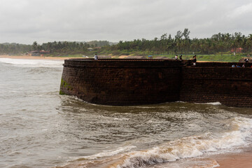 Waves crashing on the Sinquerim fort with the beach landscape in the background in Goa