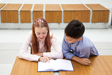 Children, schoolchildren, teenagers read in schoolyard of school on wooden bench. boy and girl are passionate about the book