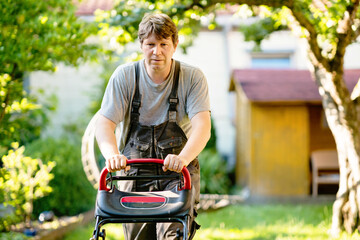 Happy young man with lawn mower. Portrait of smiling man working in garden, trimming grass. Garden...