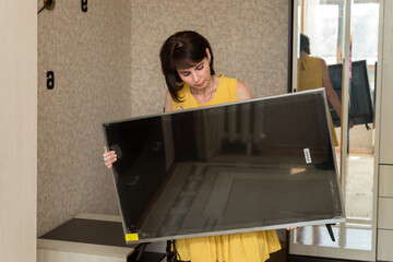 A brunette woman in a yellow dress brings a new large LCD TV into the apartment.