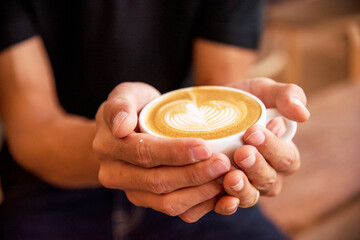 Close up hands of man sitting office desk holding sweet coffee cup relax and enjoy with happy time. Hot coffee mug in hand. Man holding coffee cup relaxing after work at office warm taste in cafe