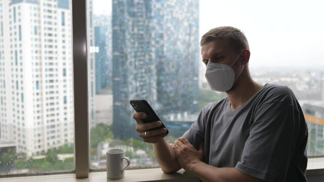 Bored and lonely white man in a face mask going through his phone while quarantining