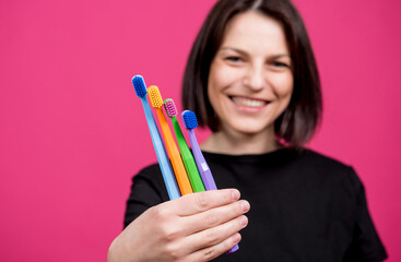 Beautiful happy young woman with different colored toothbrushes on blank pink background