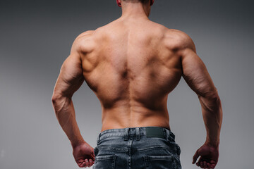 A young sexy athlete with perfect abs poses in the studio topless in jeans on the background....