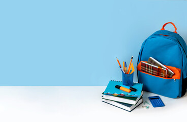 School backpack with colorful school supplies on blue background with copy space.