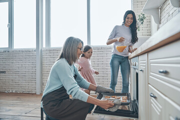 Happy senior woman taking out cookies from the oven and smiling while spending time with family