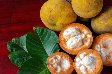 A whole bunch of santols that were cut with a knife and had leaves laid beside them in the brown wooden floor.