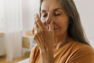 Middle-aged woman practicing yoga breathing technics at home. Elderly female breathing with one nostril. Surya bheda pranayama concept. Meditation idea - obrazy, fototapety, plakaty