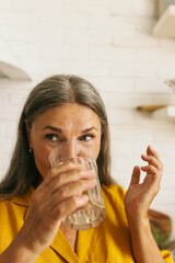 Cute middle-aged woman drinking water from glass. Mature female enjoying tasty beverage and looking...