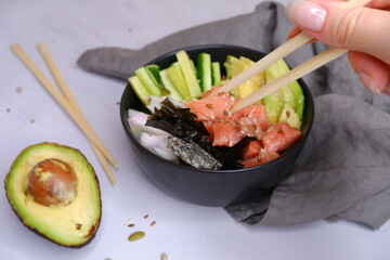 The girl eats. Poke. A plate of fish, avocado, rice.