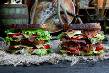 Big sandwiches with bread, prosciutto, lettuce, tomtatoes, cucumber and cheese in the kitchen
