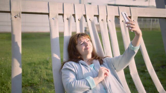 woman lies in a resting place and talking by video call on the phone, bright sunlight