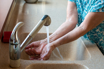 Senior woman hands under cold running water.  Close up. How to stay cool in hot weather.