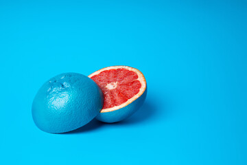 Grapefruit painted in blue and cut into halves isolated on a vibrant blue background. Tropical and...