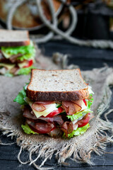 Big sandwich with bread, prosciutto, lettuce, tomtatoes, cucumber and cheese in the kitchen