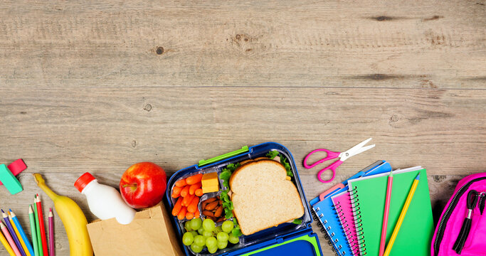 Healthy school lunch and school supplies. Top view bottom border on a wood background.