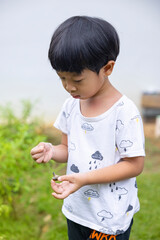 Close-up portrait Asian child boy straight black hair wearing a white white shirt and black pants, playing with snails in the vegetable section of him make funny faces of happy smiling.