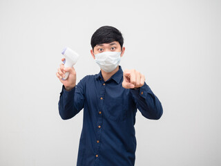 Man wearing mask hodling infrared thermometer point at you on white background isolated