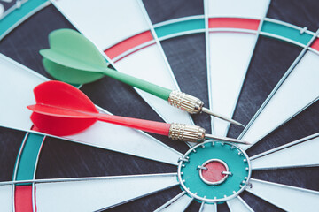 Red and Green dart arrow in on Bullseye target dartboard.