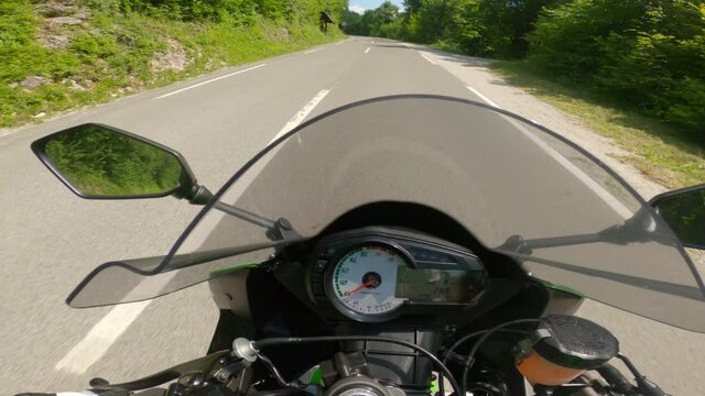 POV Motorcyclist driving on an ampty asphalt road throught the forest, slowing down on curves