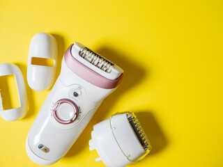 Female electric epilator in white on a yellow background. There are additional attachments nearby....