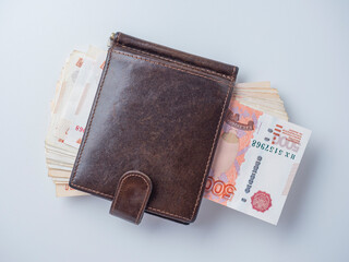 A close-up of a leather wallet full of 5000 rubles banknotes lies on a white background. Top view, flat lay