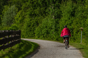 Obraz premium Path with red dressed woman on bicycle near wooden fence and color meadow