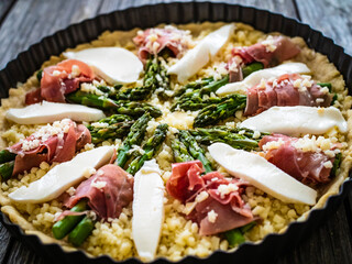 Uncooked tart with asparagus and serrano ham on wooden table
