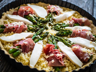 Uncooked tart with asparagus and serrano ham on wooden table
